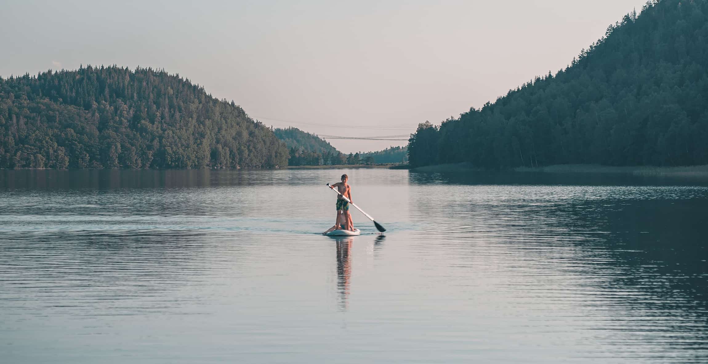En person paddlar ståpaddelbräda på en stilla sjö nära Sju Sjöar